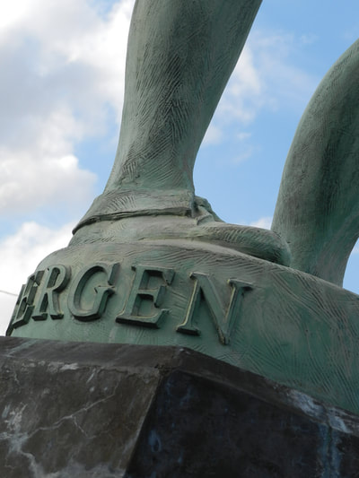 Close-up of McPherson Ad Astra's right foot in moccasin over the pedestal which sports lifted text on the back that spells the artist's name "BERGEN".