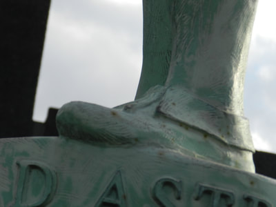 Close-up of the McPherson Ad Astra figure's left foot clad in moccasin above the pedestal base front which reads "AD ASTRA".