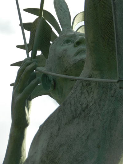 Close-up of the McPherson Ad Astra figure's face, gaze lifted toward the sky as his right hand draws the bowstring past his ear.