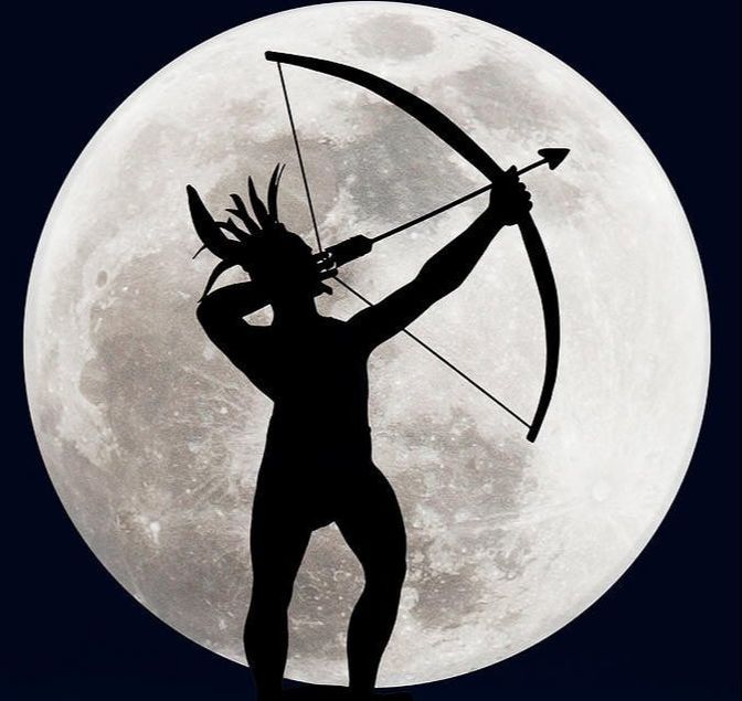 Ad Astra statue silhouetted in front of the super moon, aiming a drawn bow toward the sky at a gentle angle.