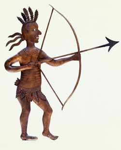 A hammered copper Indian weathervane with small pieces of glass for eyes depicts a Native American man in loincloth and with five feathers atop his head, aiming a bow and arrow at a slightly upward angle.